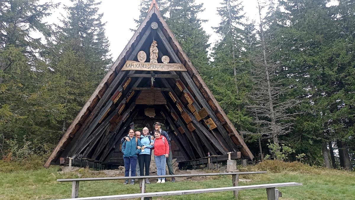 Grupa uczestników rajdu stoi pod drewnianą wiatą